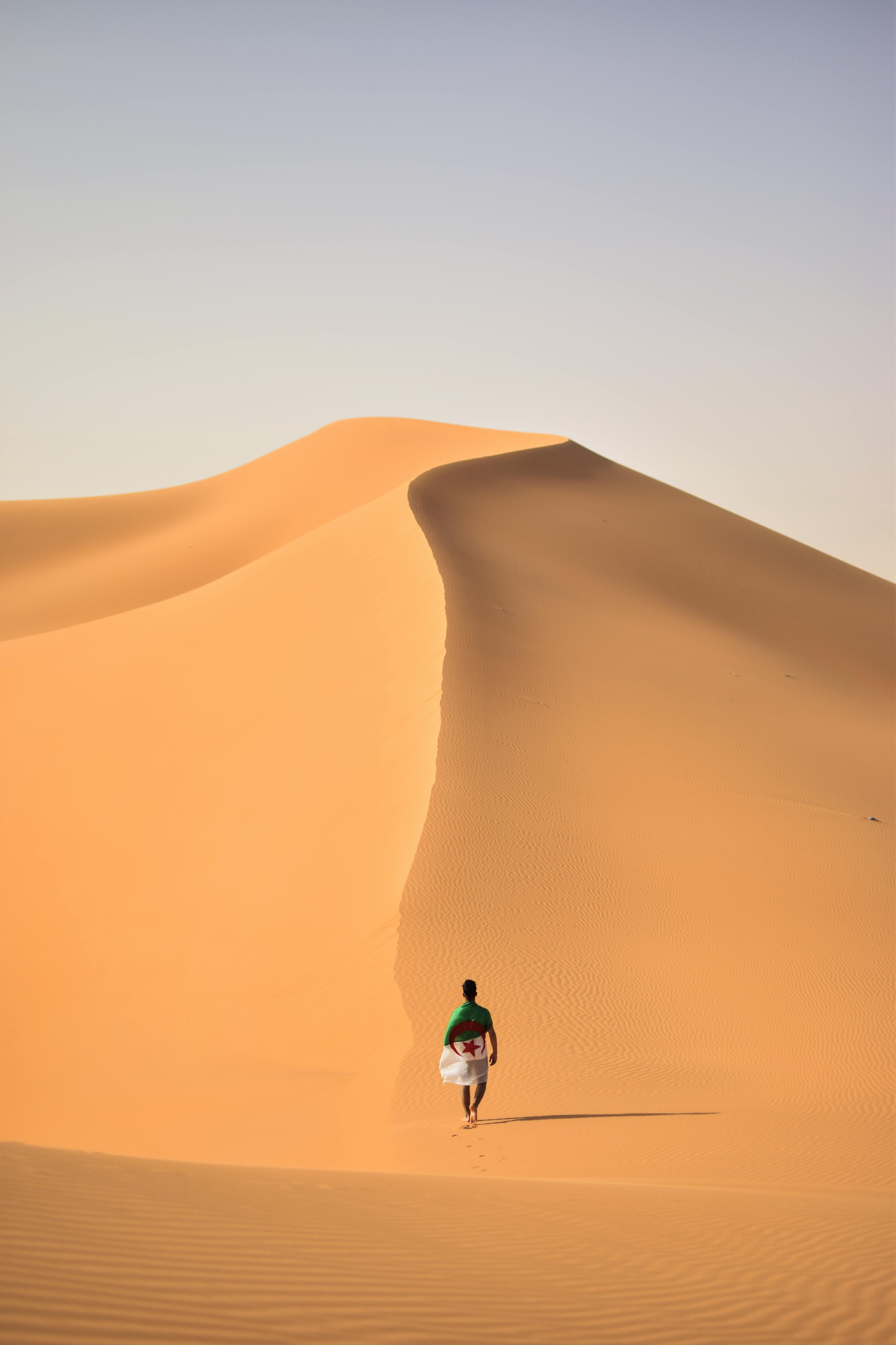 A man is walking up a sand dune in the desert.