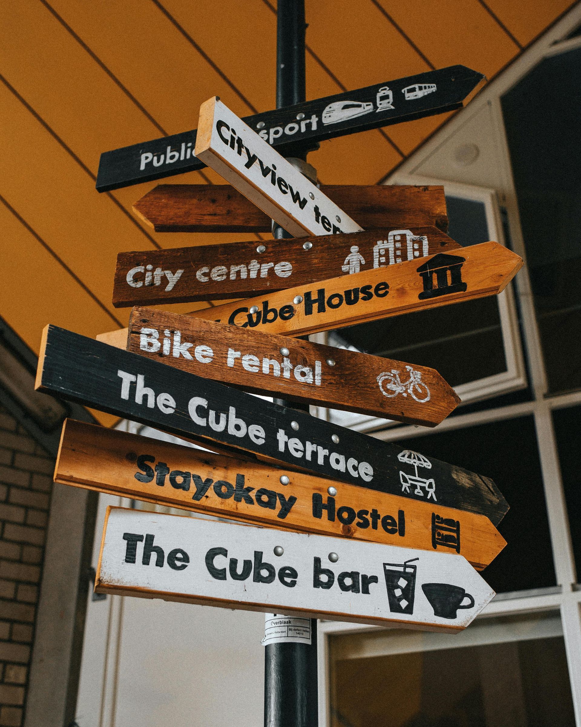 A stack of street signs pointing in different directions including the cube bar