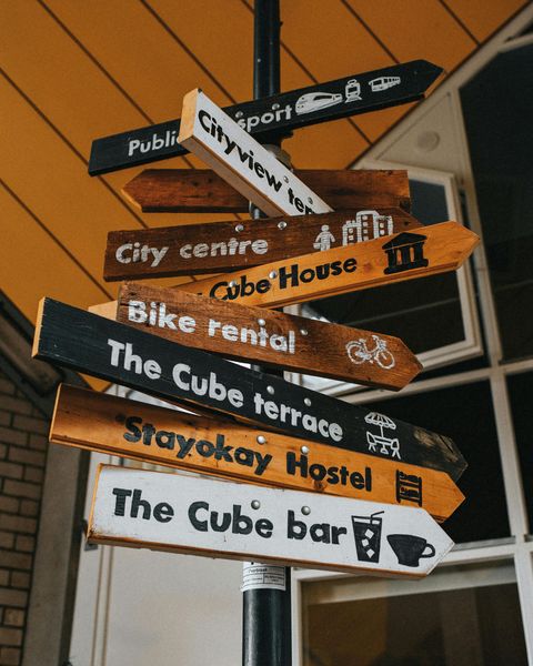 A stack of street signs pointing in different directions including the cube bar