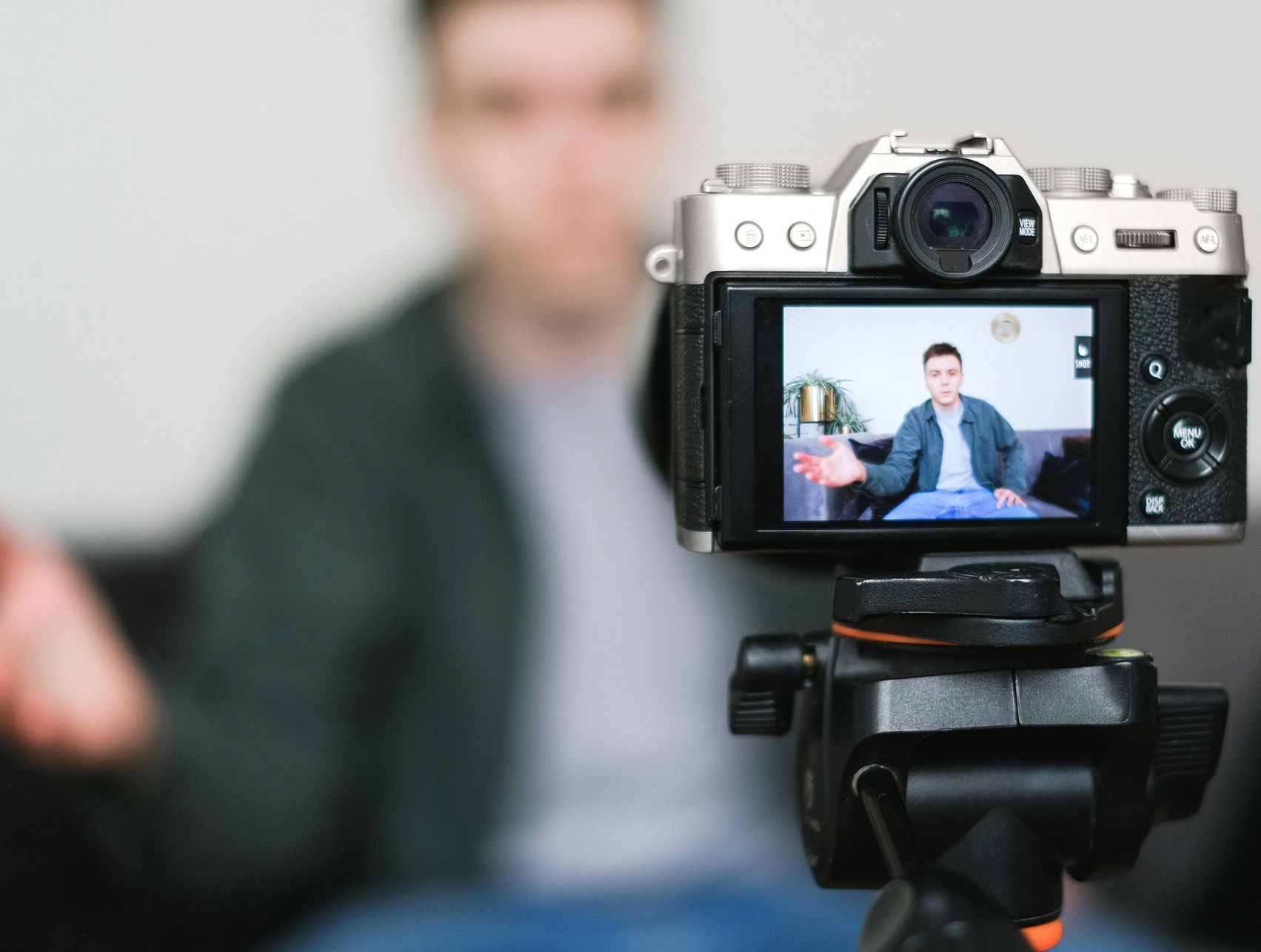 A man is sitting on a couch being filmed by a camera.