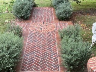 A brick walkway surrounded by shrubs and grass in a garden.