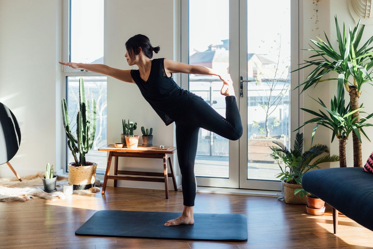 A woman is doing a yoga pose on a mat in a living room.