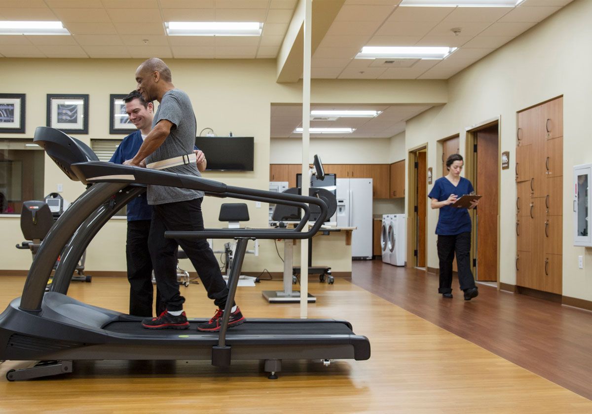 A man is walking on a treadmill while a nurse looks on.