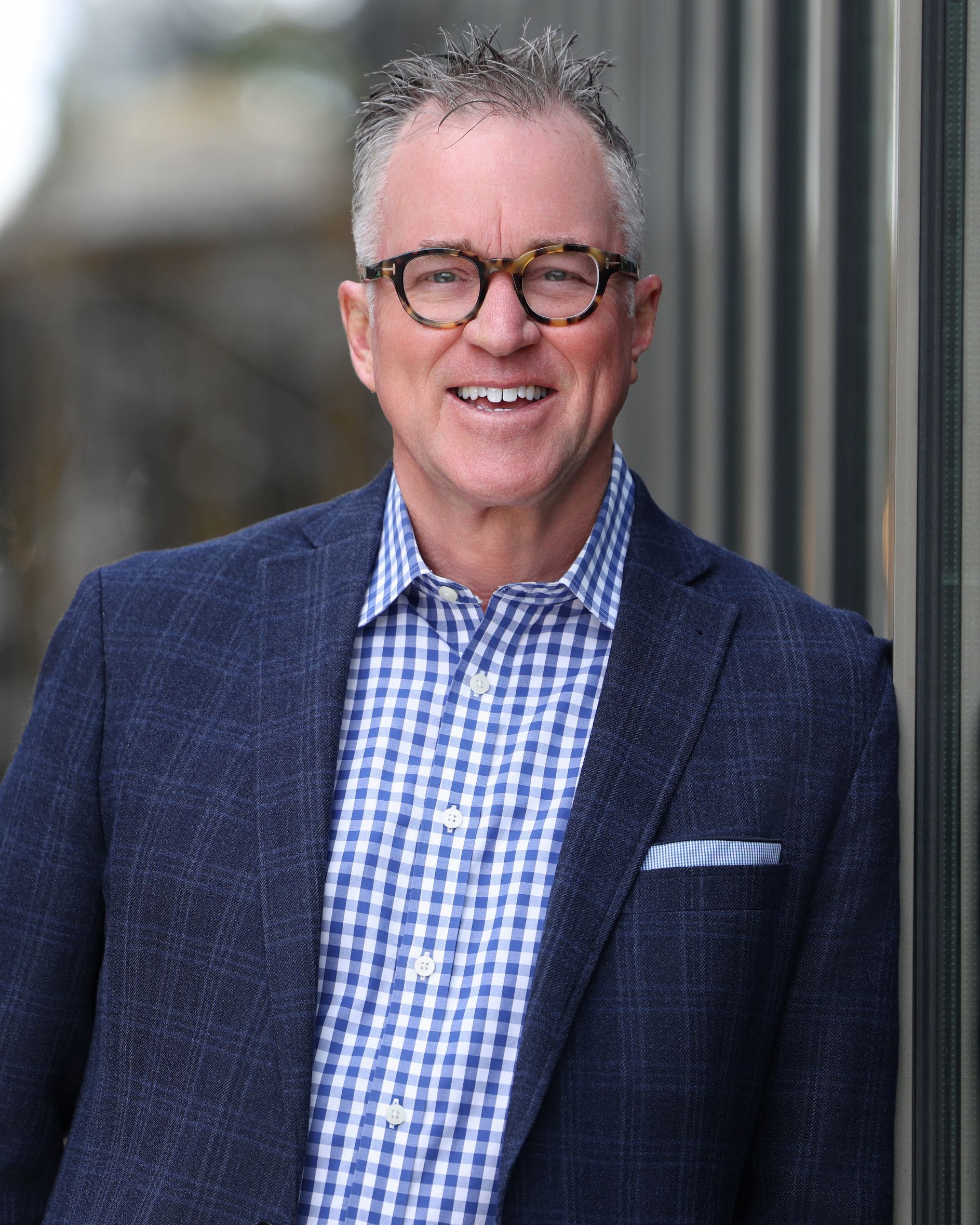 A man in a suit and glasses is standing with his arms crossed and smiling.