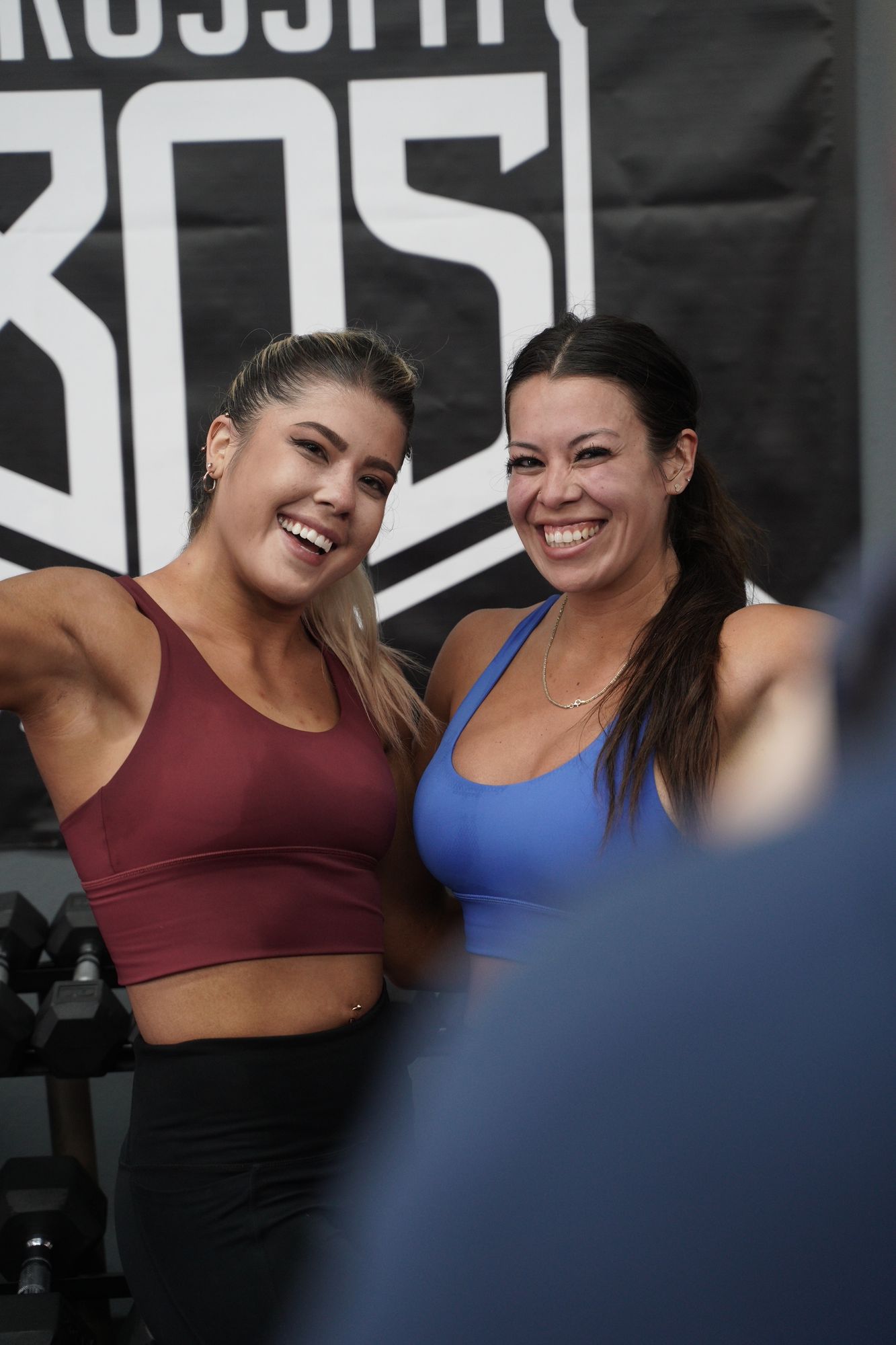 Two smiling women in workout clothes pose for a photo at a gym.