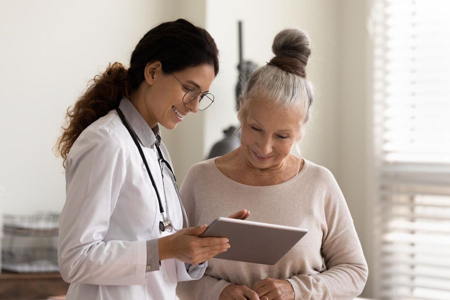 Doctor showing a tablet to an elderly patient; they are both looking at the screen indoors.