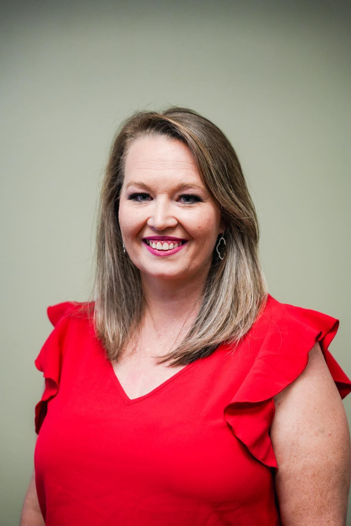 Woman in a red dress smiles at the camera. Beige wall in the background.