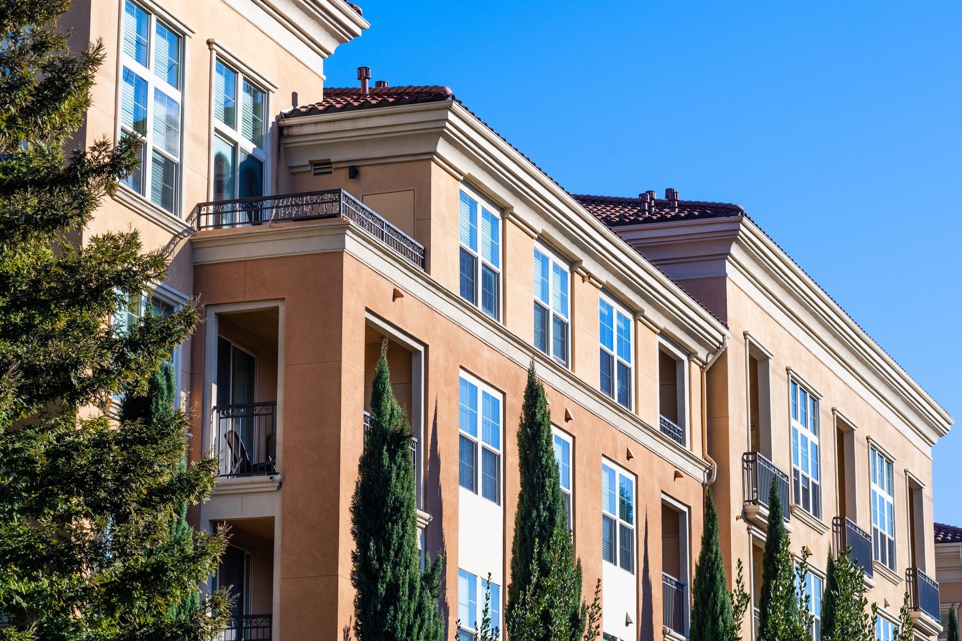 Multi-story beige apartment building with balconies and blue sky.