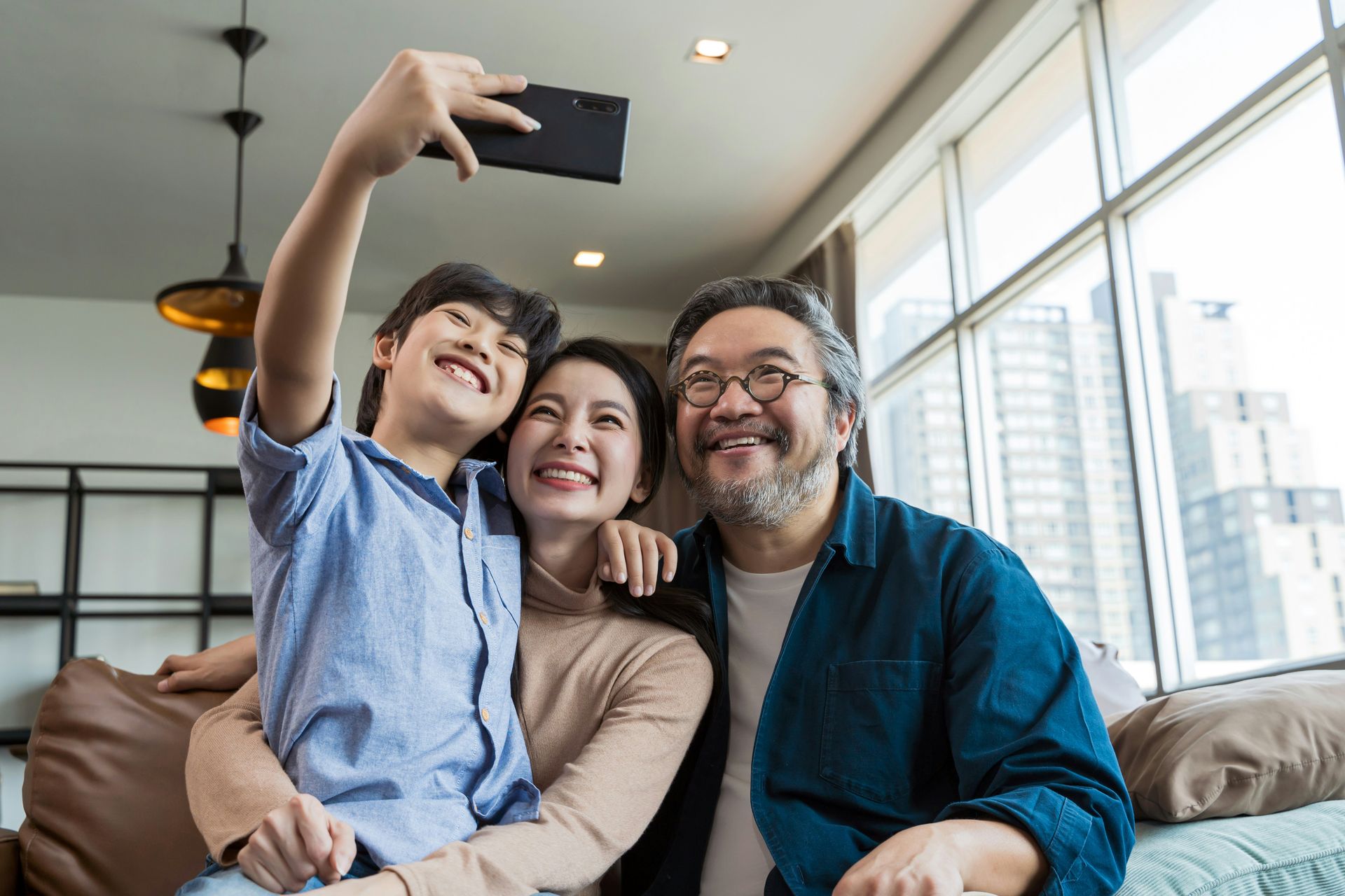 Family, smiling, taking a selfie indoors. Boy holding the phone, mom and dad posing.