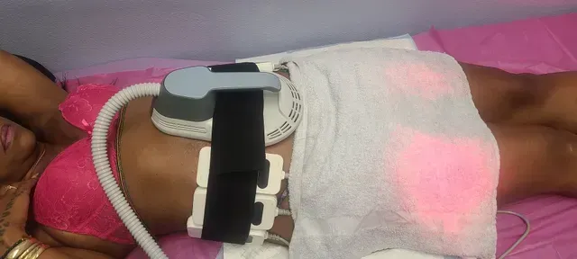 A woman is laying on a bed with a machine on her stomach.