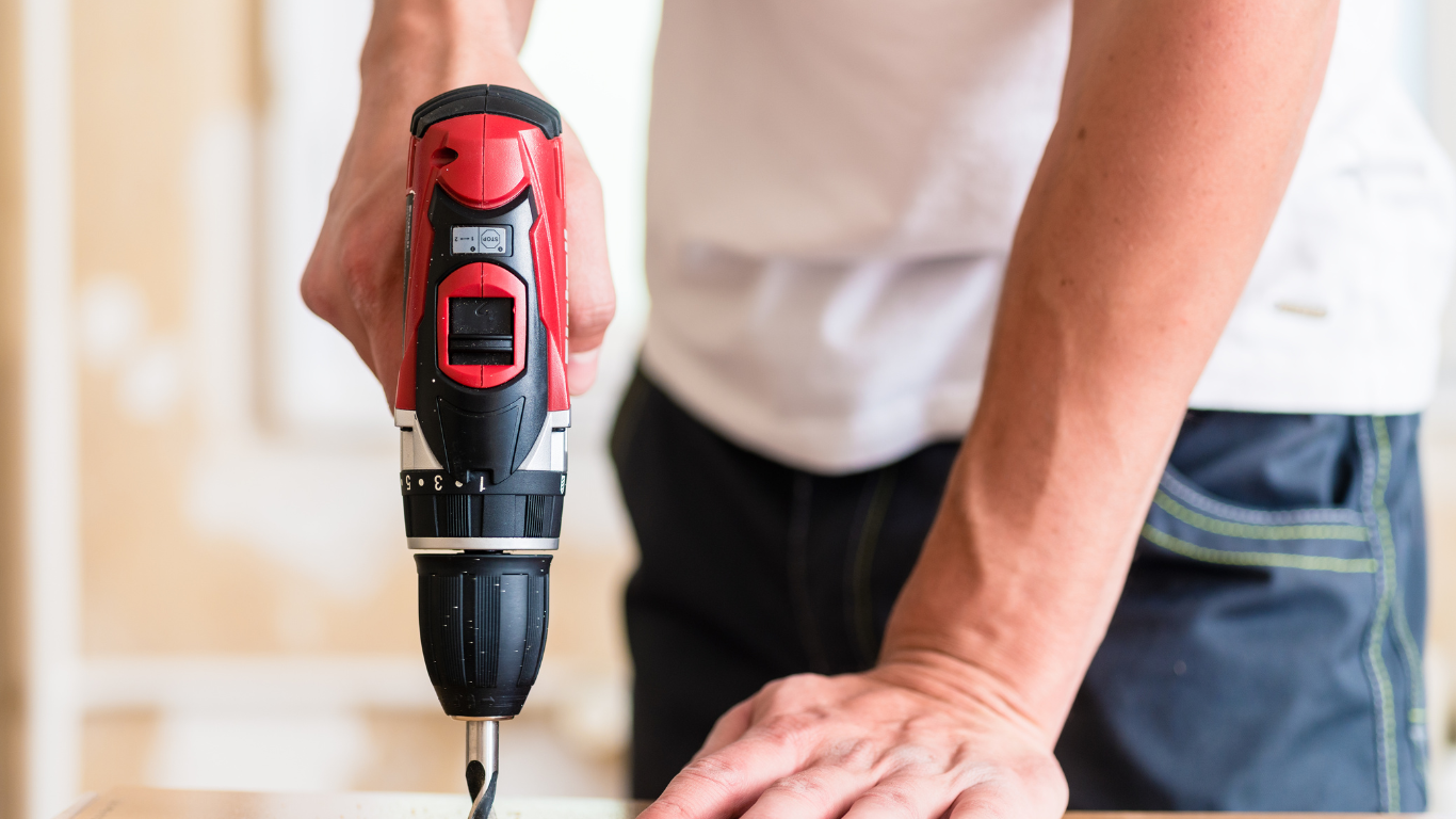 A man is using a drill to drill a hole in a piece of wood.