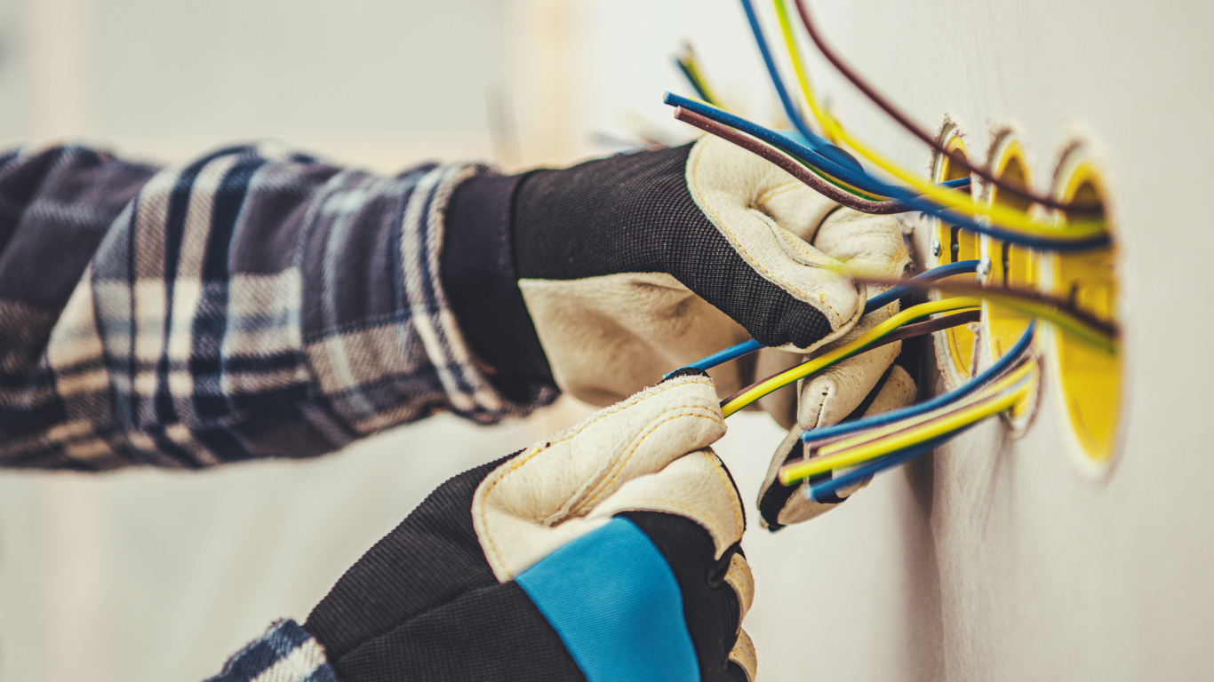 A man is installing electrical wires in a wall.