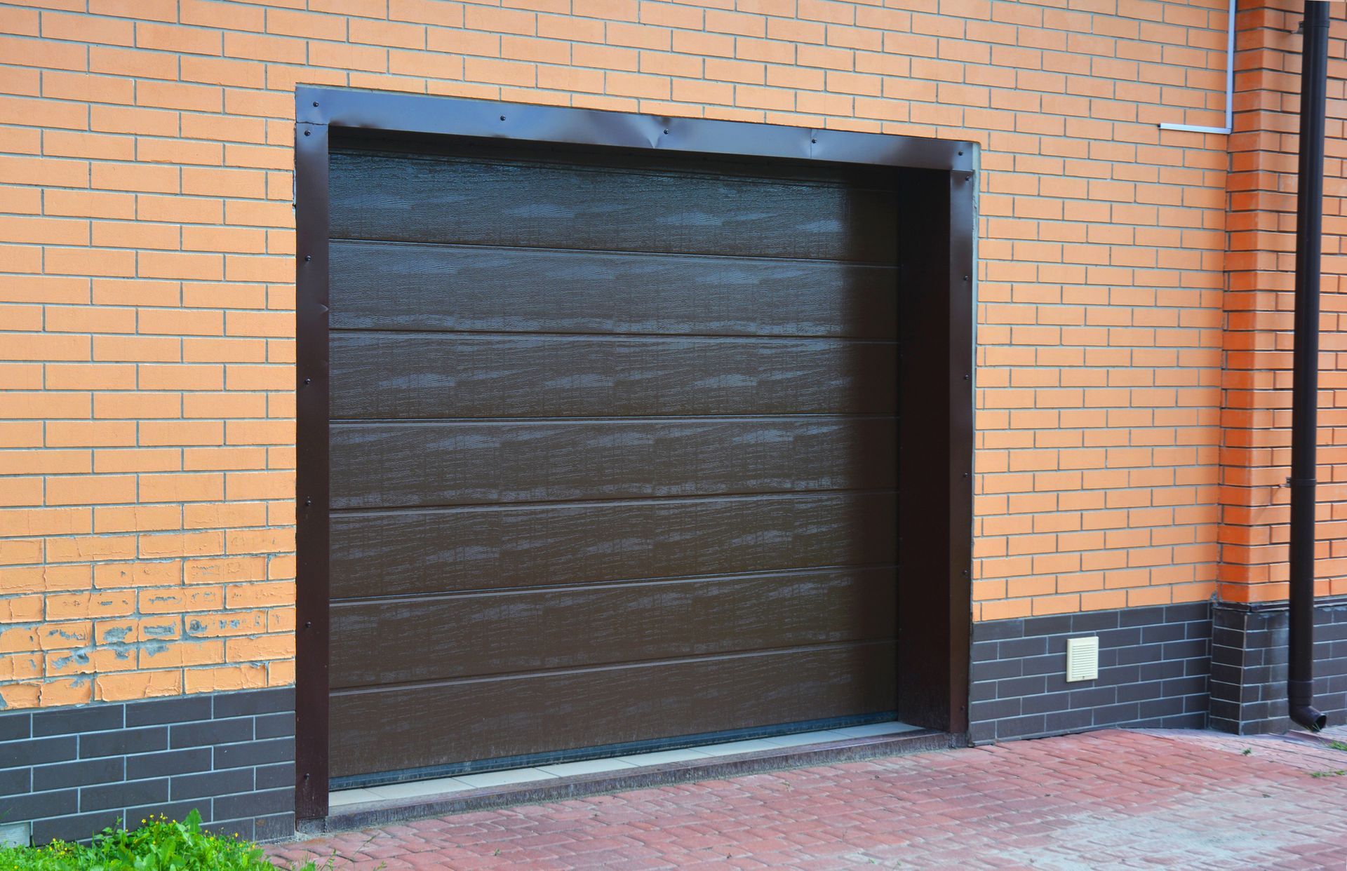 Black garage door in brick wall and floor, representing local garage door repair services.