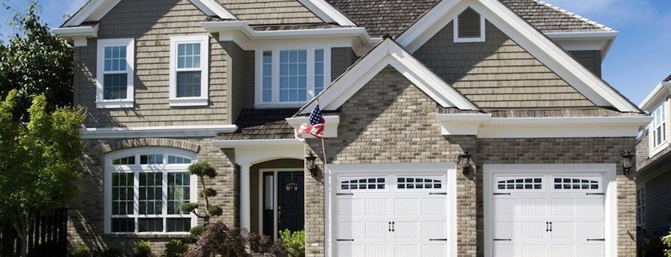 A large brick house with two white garage doors and an american flag