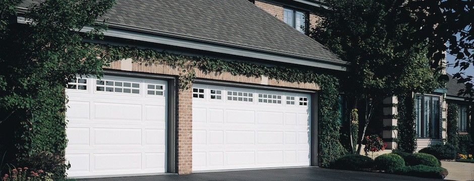 A house with two white garage doors is surrounded by trees