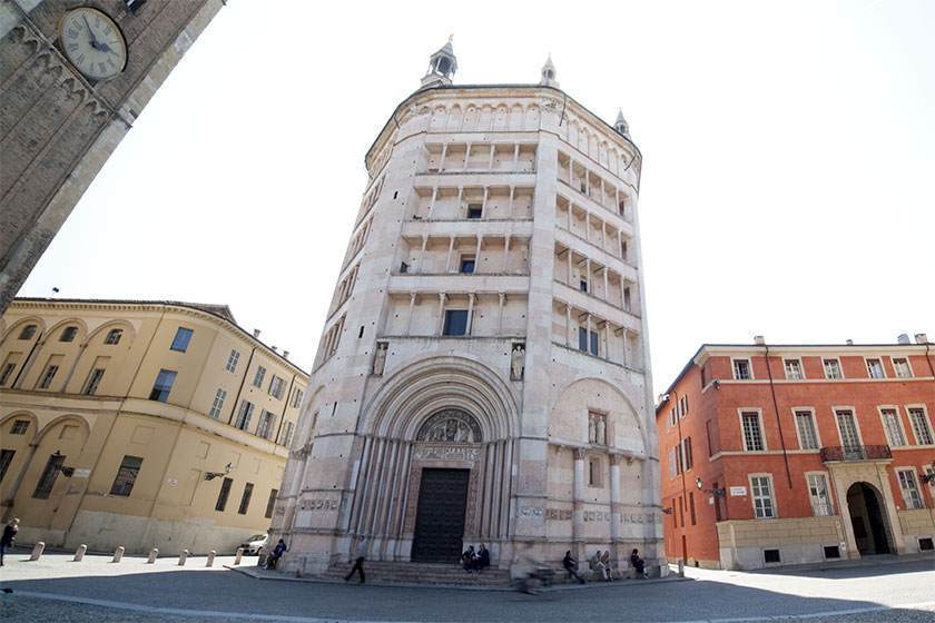 Octagonal marble baptistery in Parma, Italy, with arched entrance and surrounding buildings.