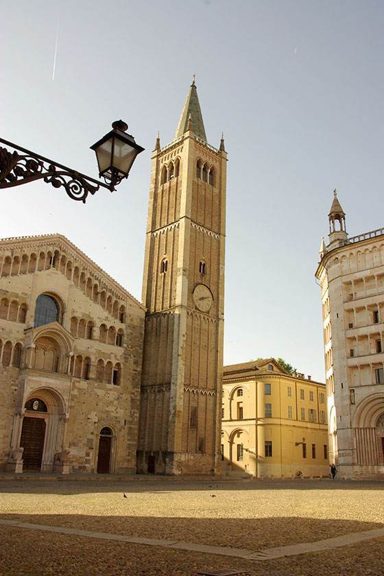 A tall brick bell tower and cathedral in Parma, Italy, under a clear sky.