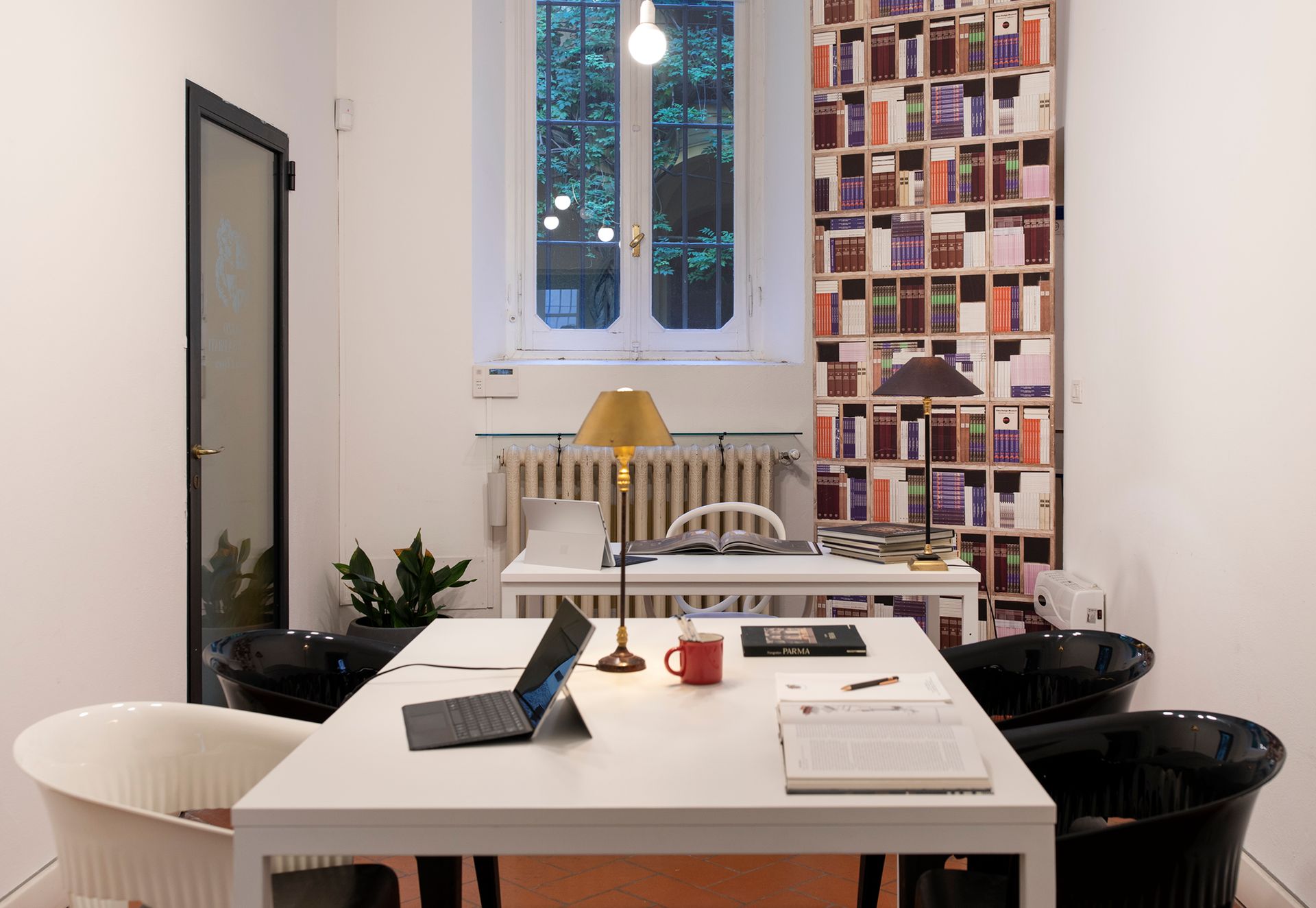 An office with a large white desk, chairs, lamps, a window, and art on the wall.