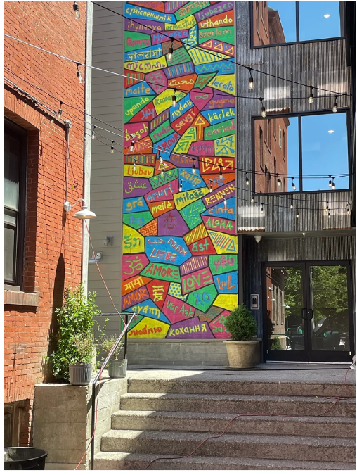 A colorful mural on a building exterior with steps leading to the entrance. Brick building on the left.