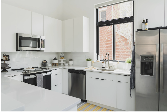 White kitchen with stainless steel appliances, window, and countertop.