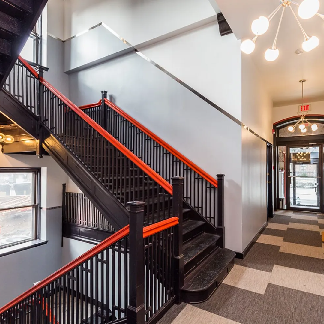 Staircase with black railing, orange accents, gray walls, and patterned carpet leading to an entrance.