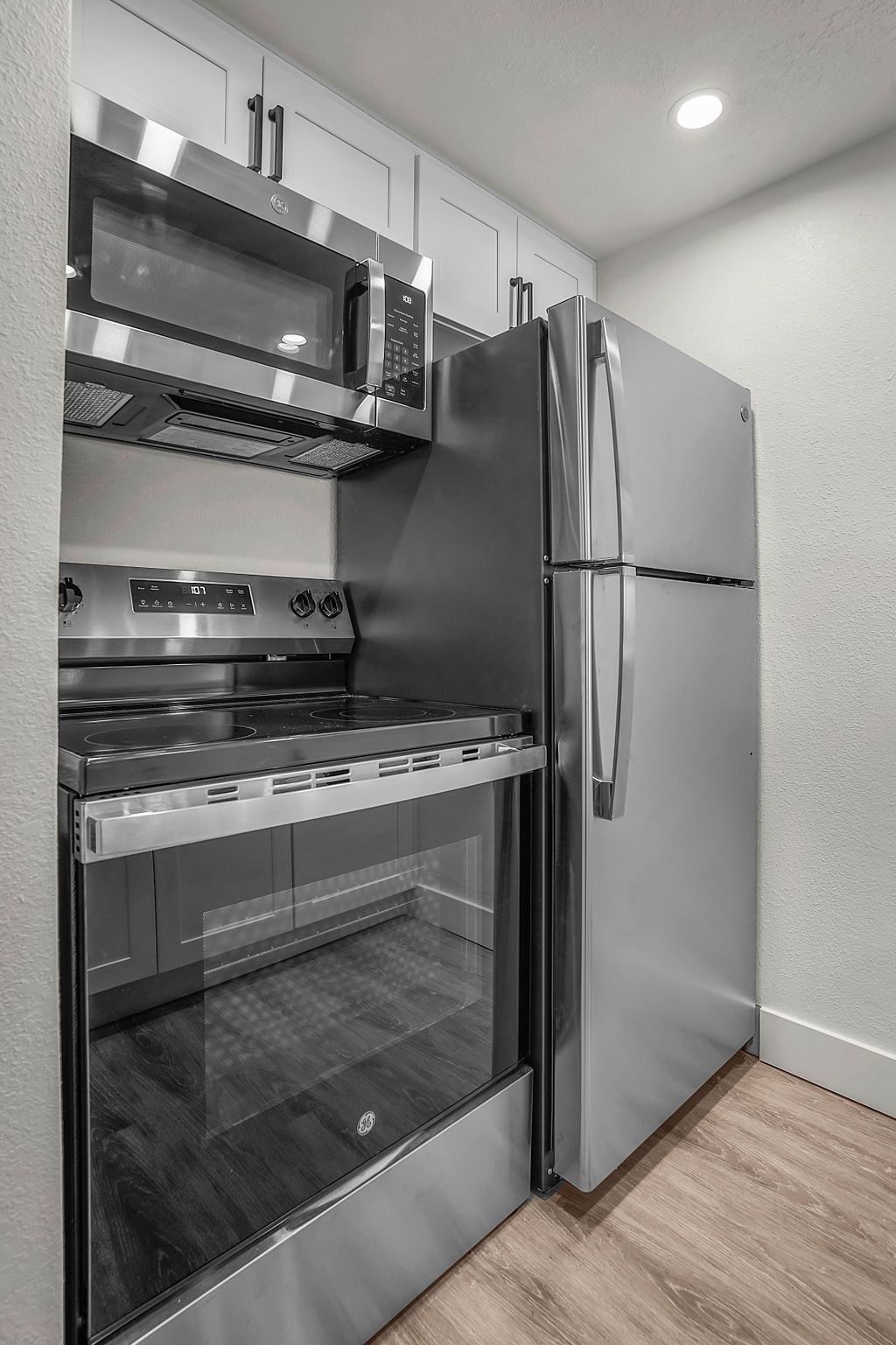 Small kitchen with stainless steel appliances: refrigerator, oven, microwave. Light wood floor, white cabinets.
