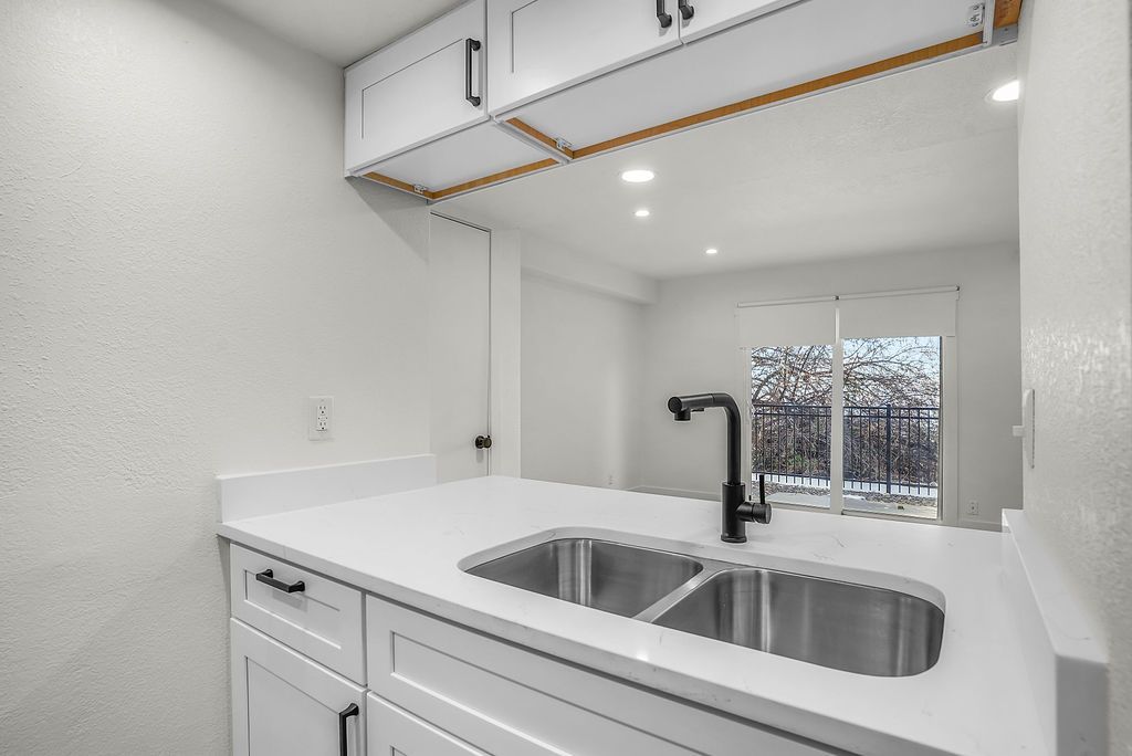 Kitchen with white cabinets, countertops, and a double sink. Black faucet and hardware. Sliding door in the background.