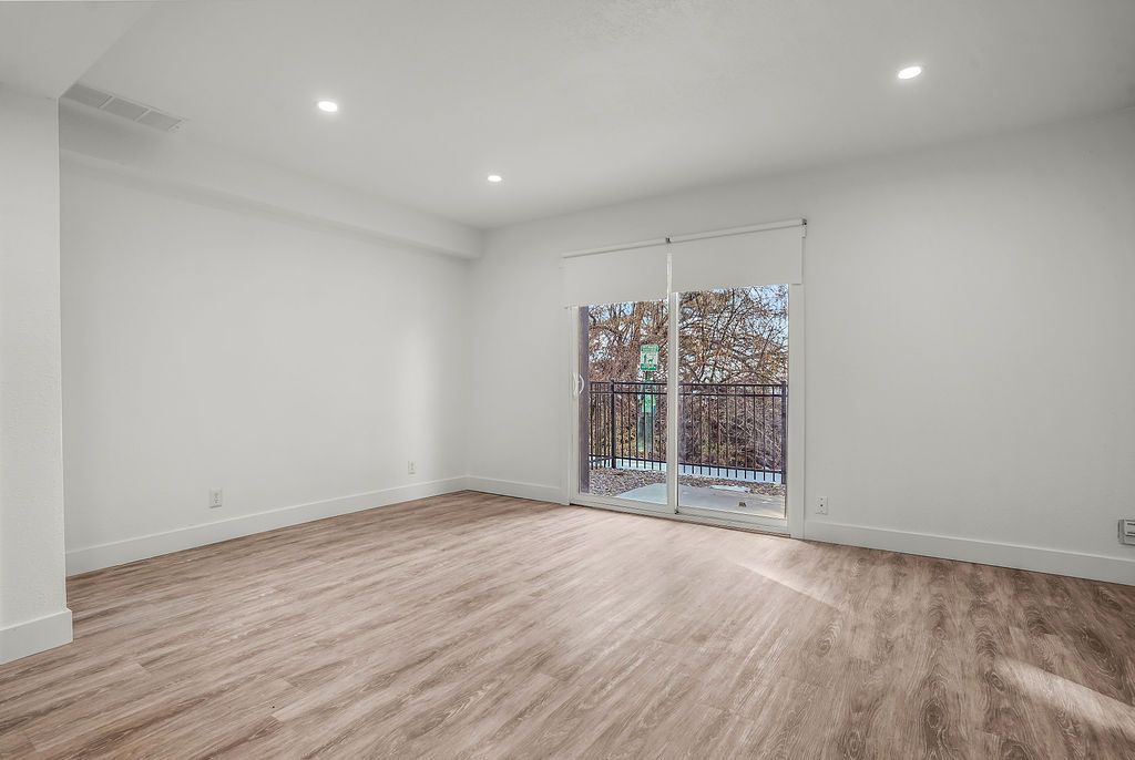 Empty room with wood-look floor, sliding glass doors, white walls, and recessed lighting.