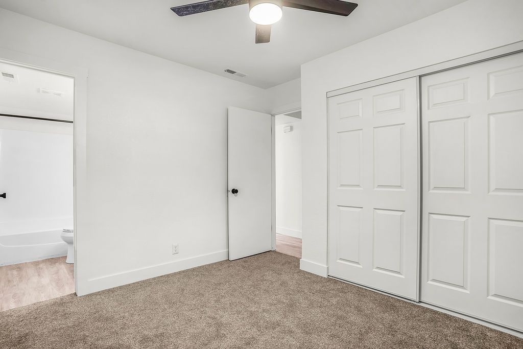 Empty bedroom with white walls, closet doors, and carpet. Doorways to bathroom and hallway.
