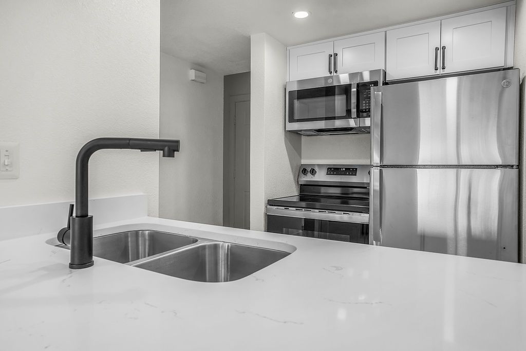Modern kitchen with white countertops, stainless steel appliances, and black faucet.