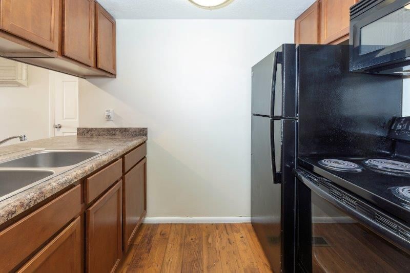 Kitchen with brown cabinets, stainless steel sink, black appliances, and wood-look flooring.