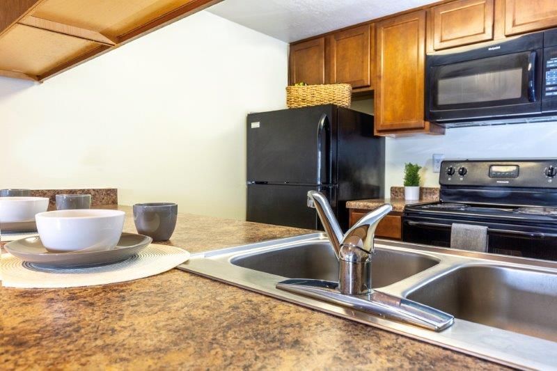 Kitchen with brown countertops, stainless steel sink, black appliances and wood cabinets.
