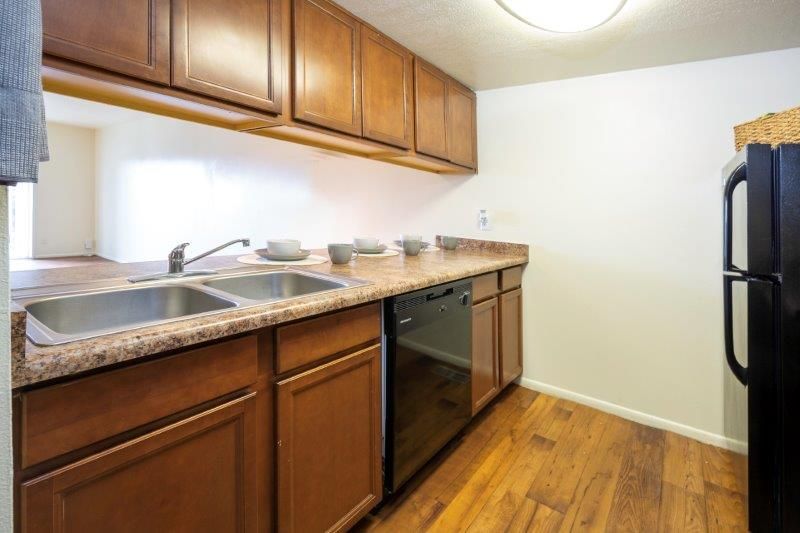 Kitchen with wooden cabinets, countertop, and appliances. View into a living area beyond.