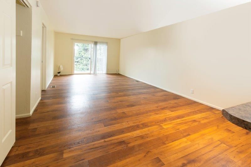 Empty living room with wood floor, sliding glass door to outside, and off-white walls.