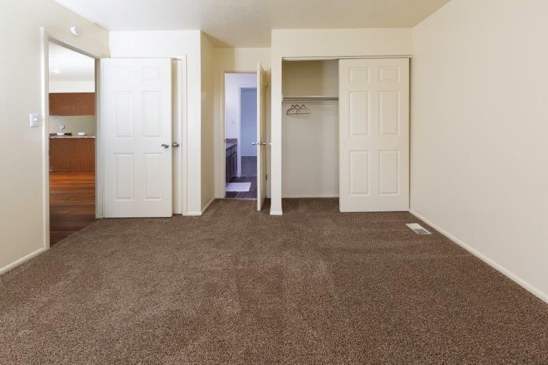Empty bedroom with brown carpet, white walls, and closet. Doors lead to other rooms.
