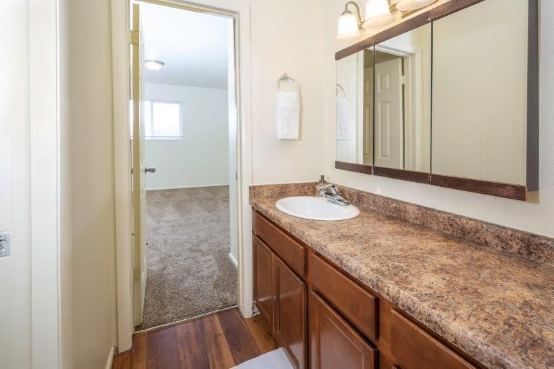 Bathroom with brown vanity, white sink, large mirror, open doorway to bedroom.