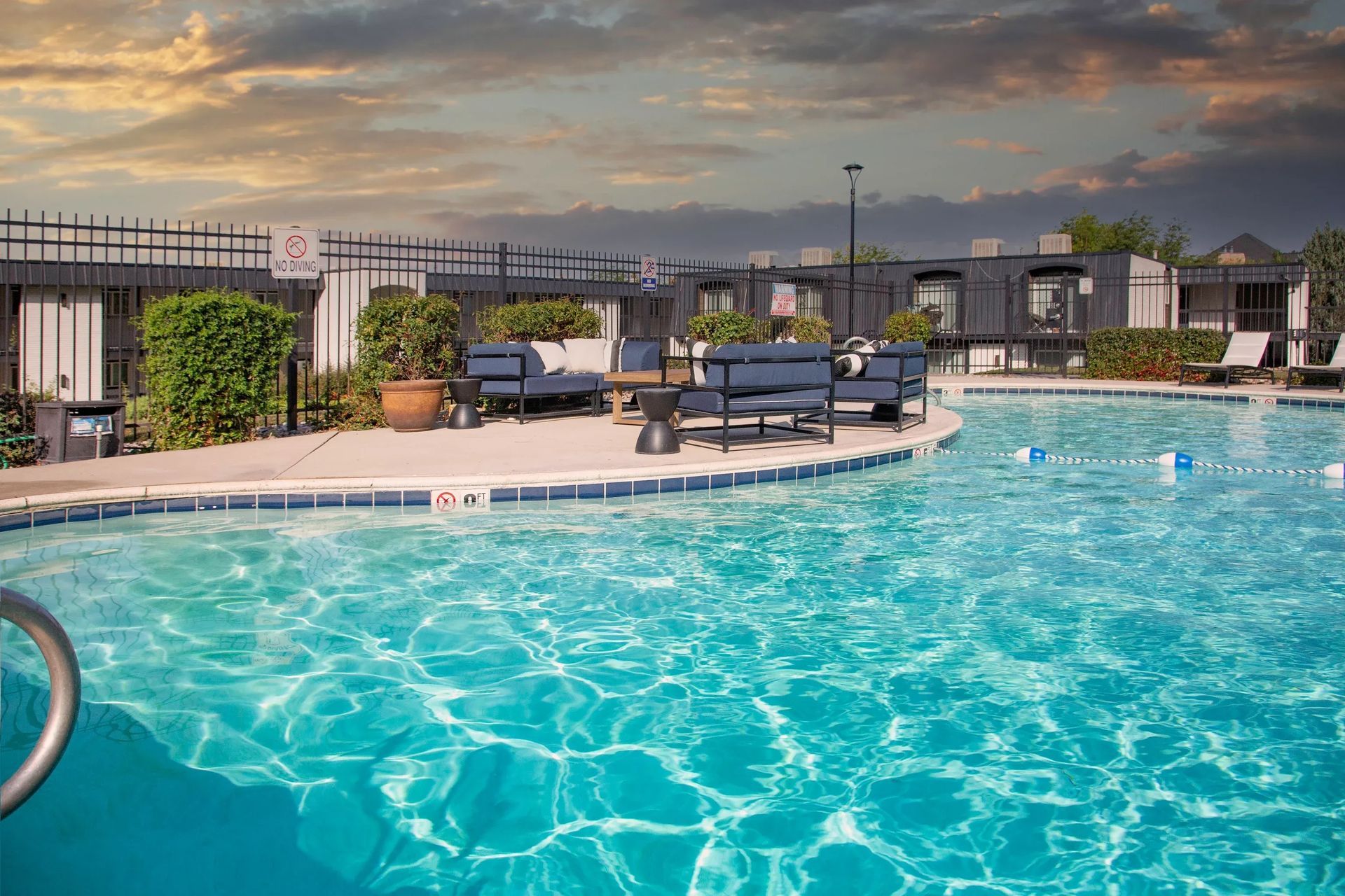 Pool with blue water, lounge chairs, and seating areas with a cloudy sky in the background.