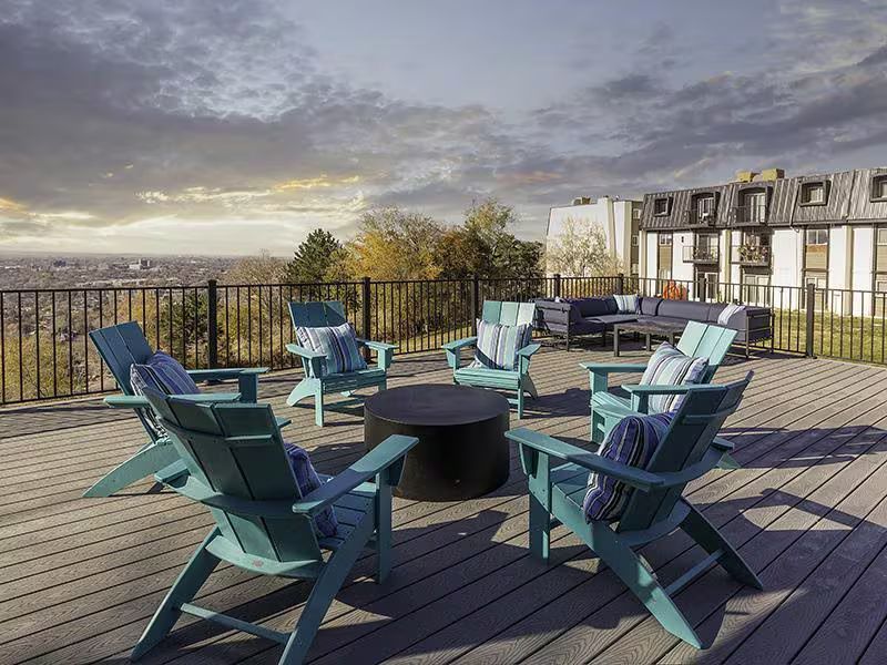 Outdoor patio with teal Adirondack chairs around a fire pit, overlooking a city view.