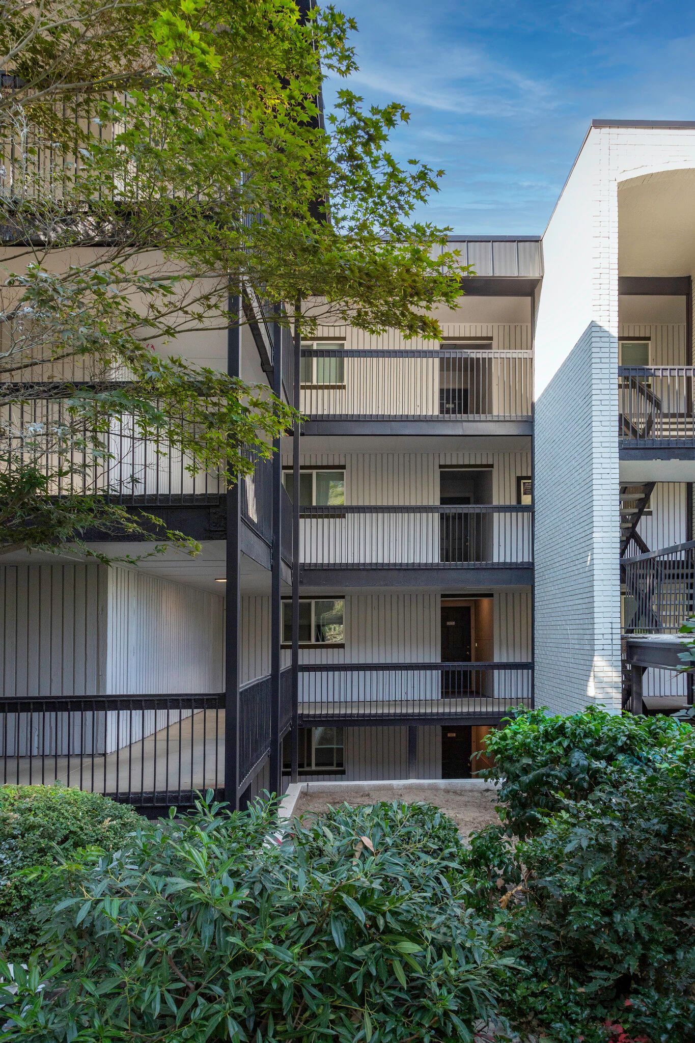 Multi-story apartment building with balconies, visible foliage, and a blue sky.