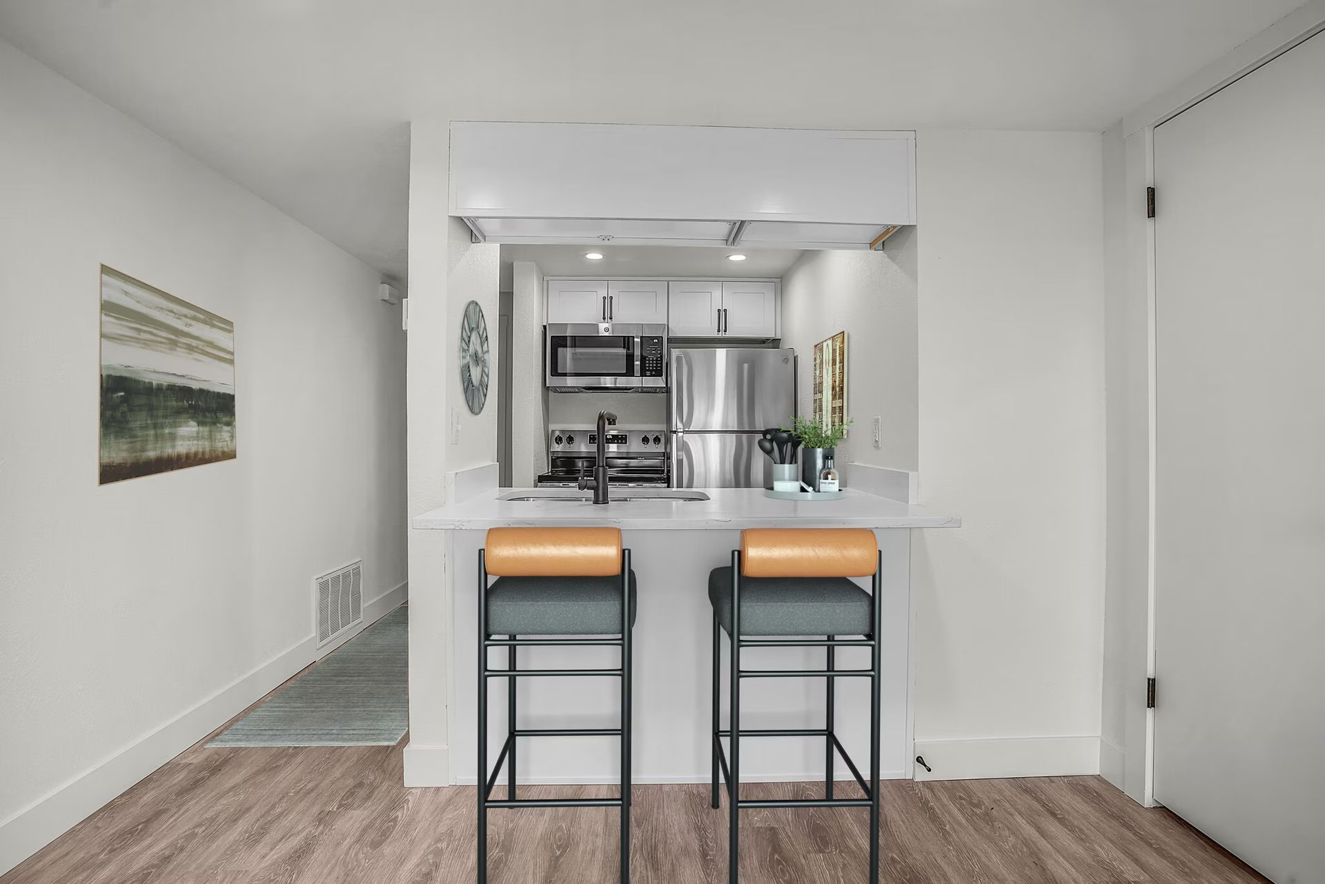 Kitchen with a breakfast bar and two stools, white cabinets, and stainless steel appliances.