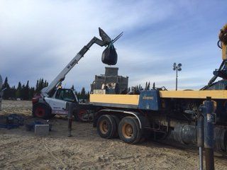 Une grue soulève un sac de béton dans un camion à benne basculante.