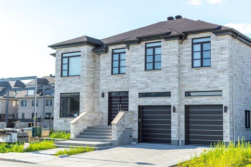Une grande maison en briques blanches avec deux garages et escaliers.