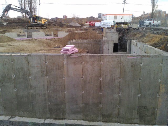 Un chantier de construction avec un mur de béton et une grande excavatrice en arrière-plan.