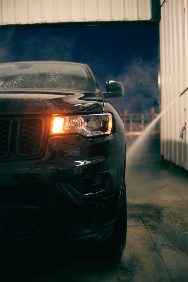 A black jeep grand cherokee is being washed with a high pressure washer.