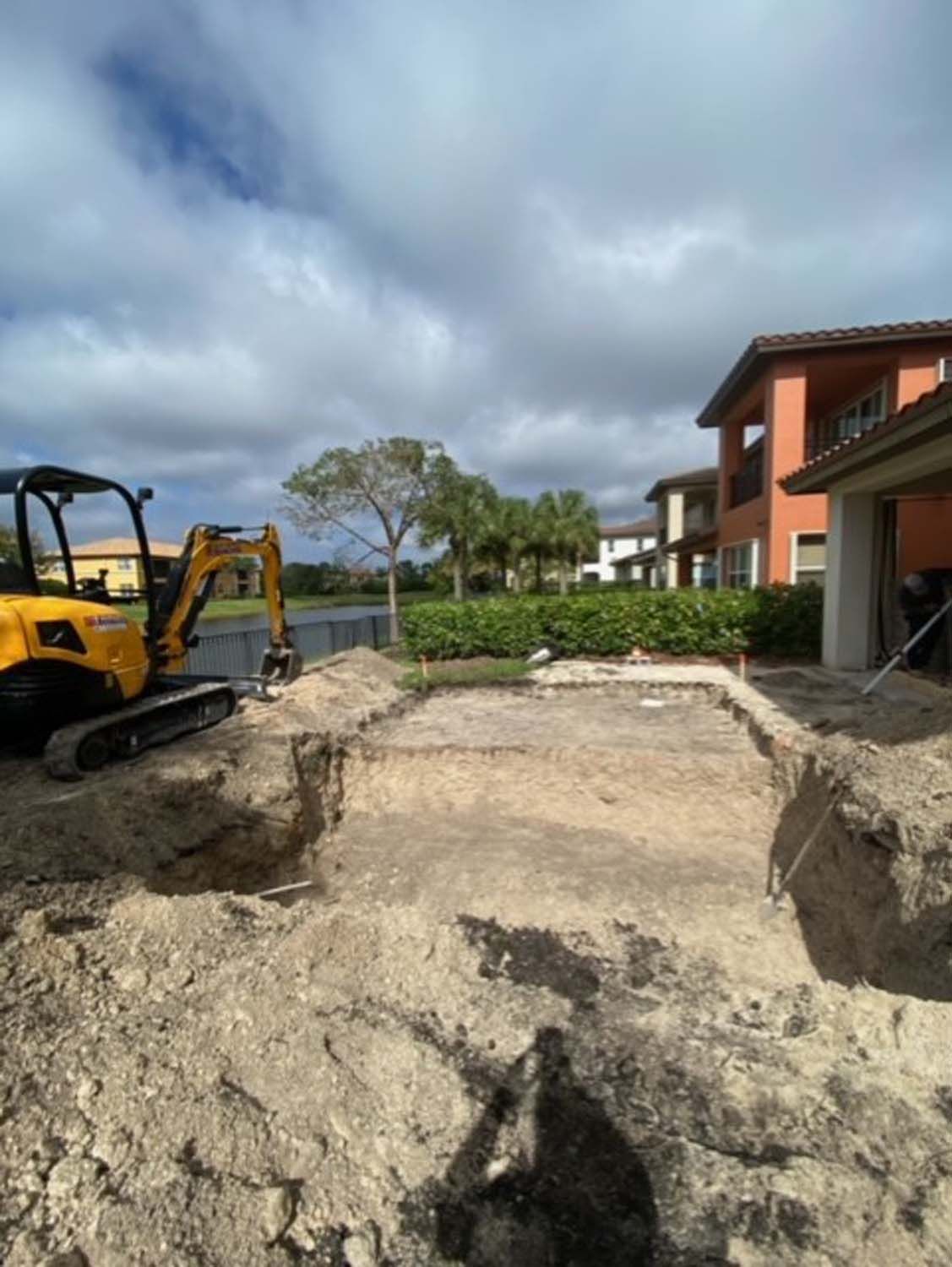 A yellow excavator is digging a hole in the ground in front of a house