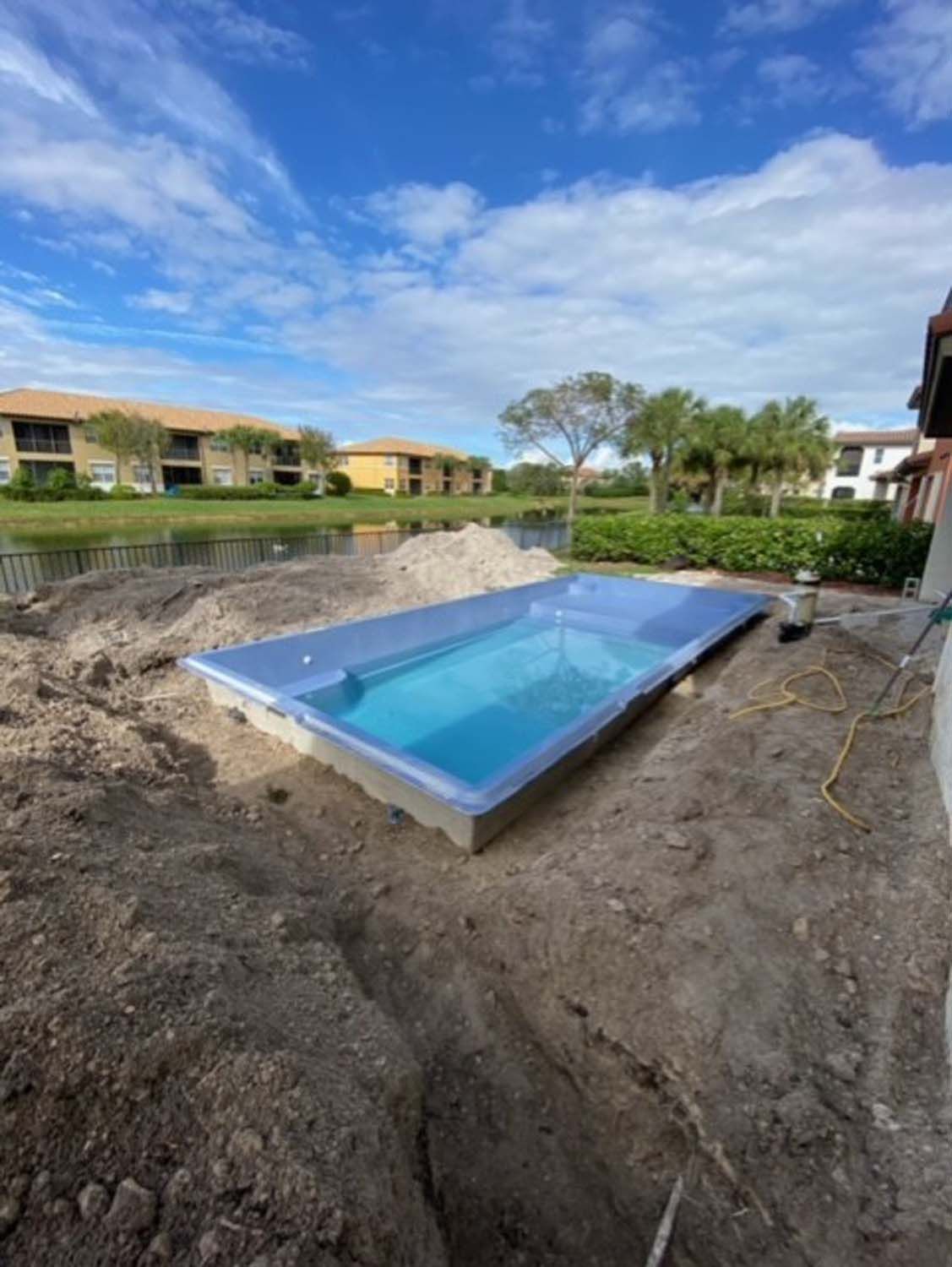 A large swimming pool is sitting in the dirt in front of a building.