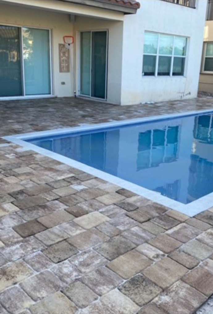 A large swimming pool with a brick patio in front of a house