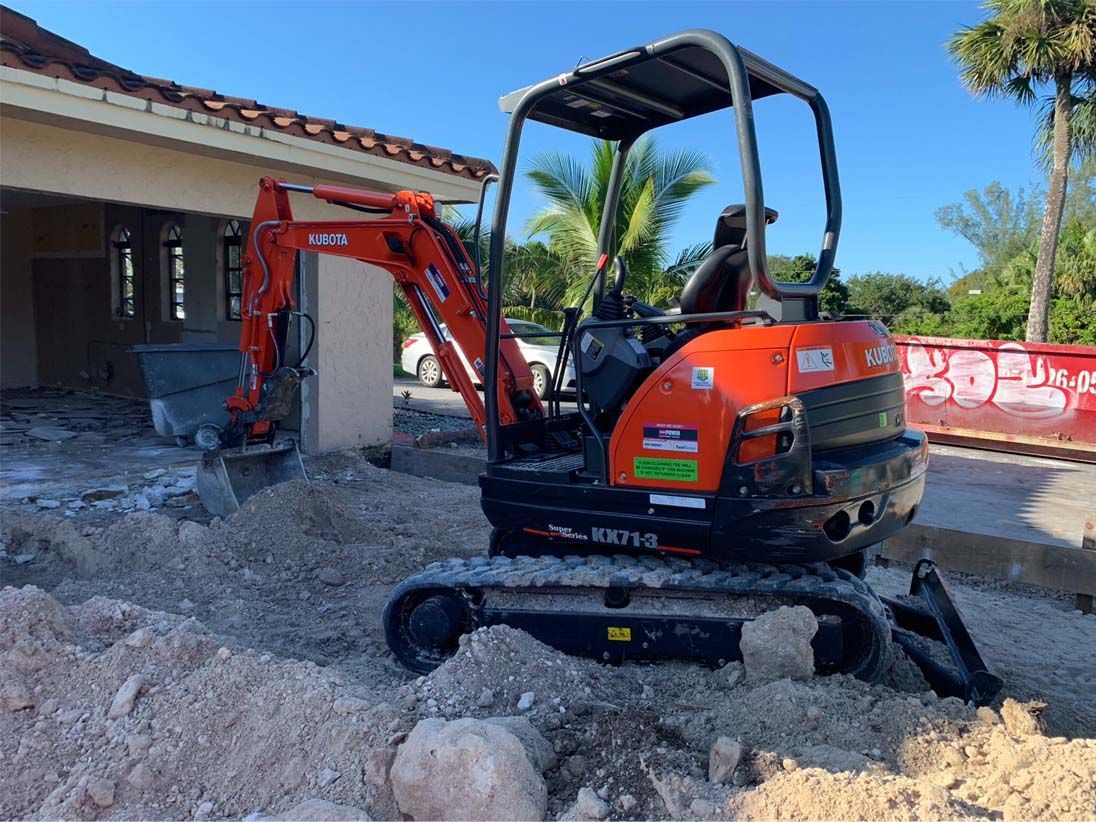 A small orange excavator is digging a hole in front of a house.