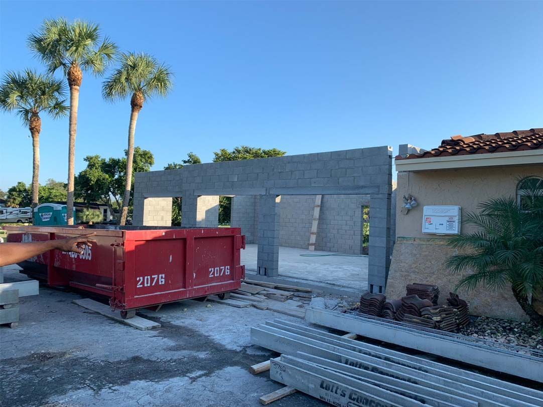 A red dumpster is sitting in front of a house under construction.