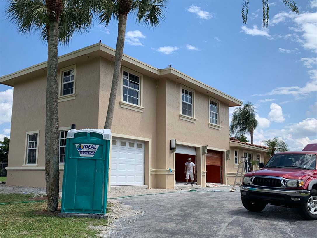 A green portable toilet is parked in front of a house.